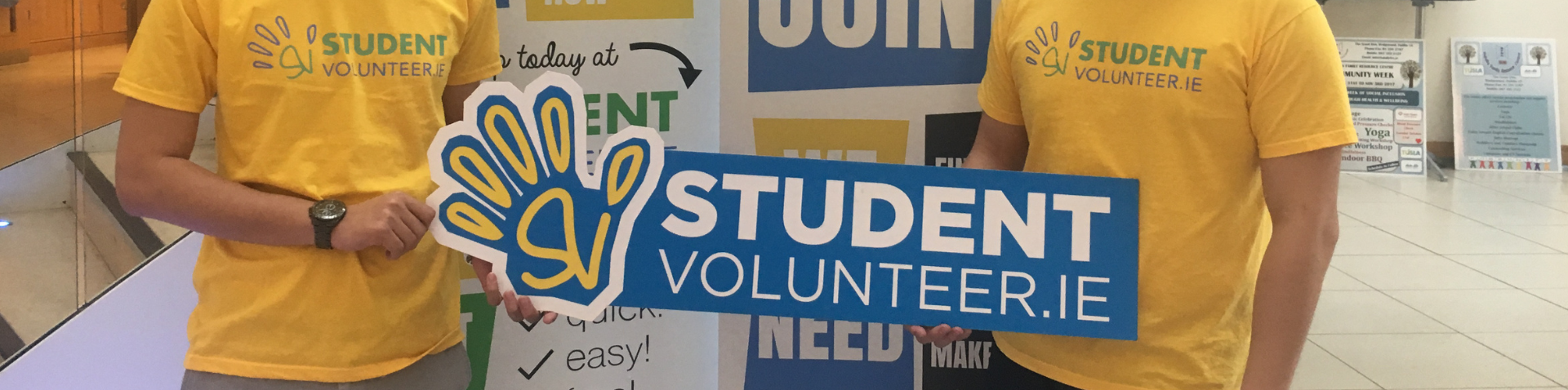 Two students standing in front of a UCD in the Community banner holding a StudentVolunteer.ie sign
